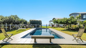 Una piscina rectangular con un banco en el centro, rodeada por una valla de madera y sillas.