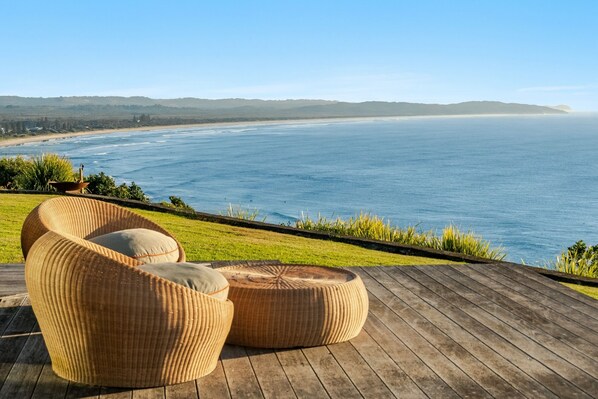 A wooden deck with wicker furniture overlooking a beach.