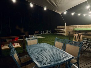 Une terrasse extérieure avec une table et des chaises en métal, entourée d’une plateforme en bois et d’une pelouse.