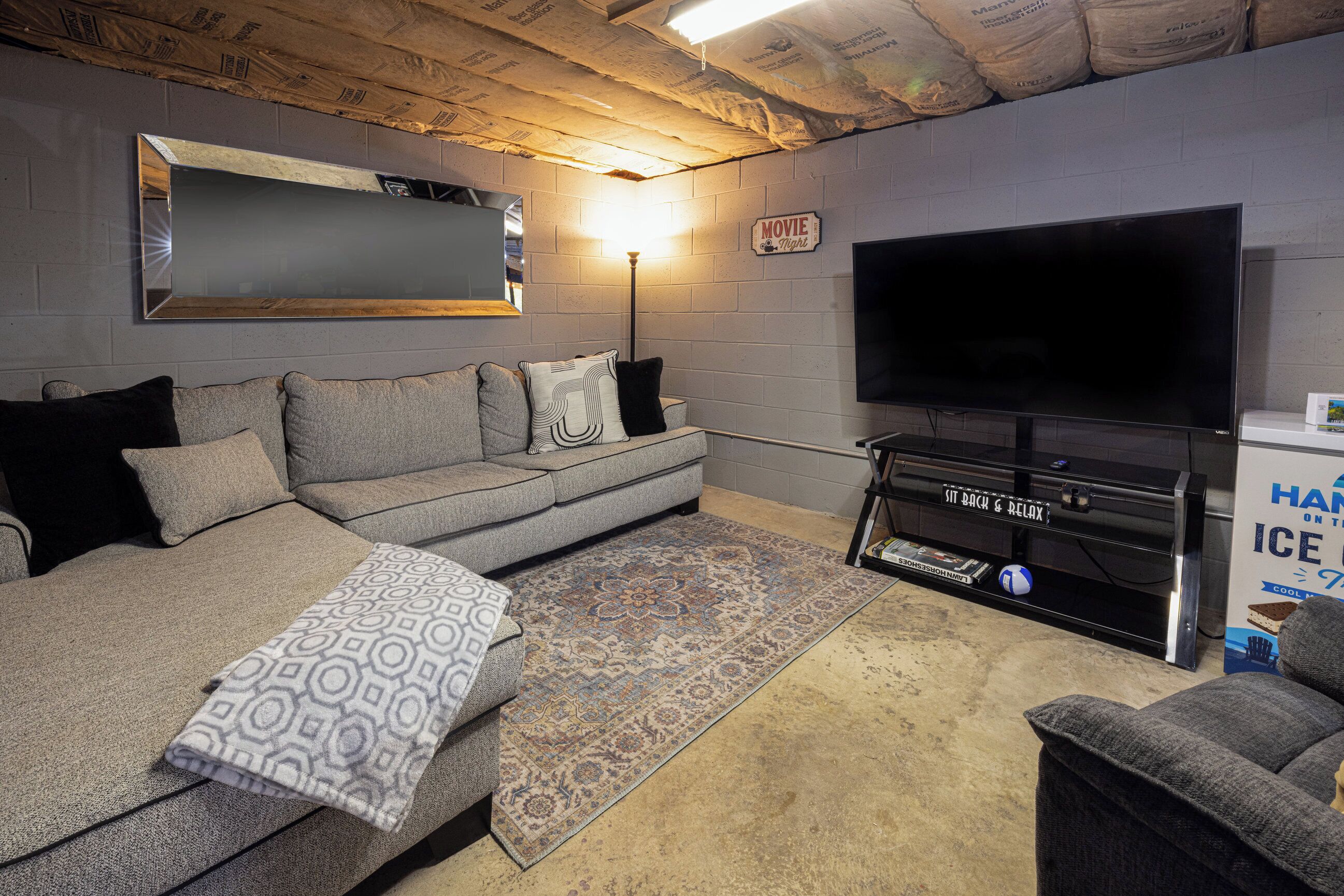 Uma sala de estar com um sofá cinza, uma TV de tela plana, um tapete estampado e um letreiro que diz 'NOITE DE FILME'.