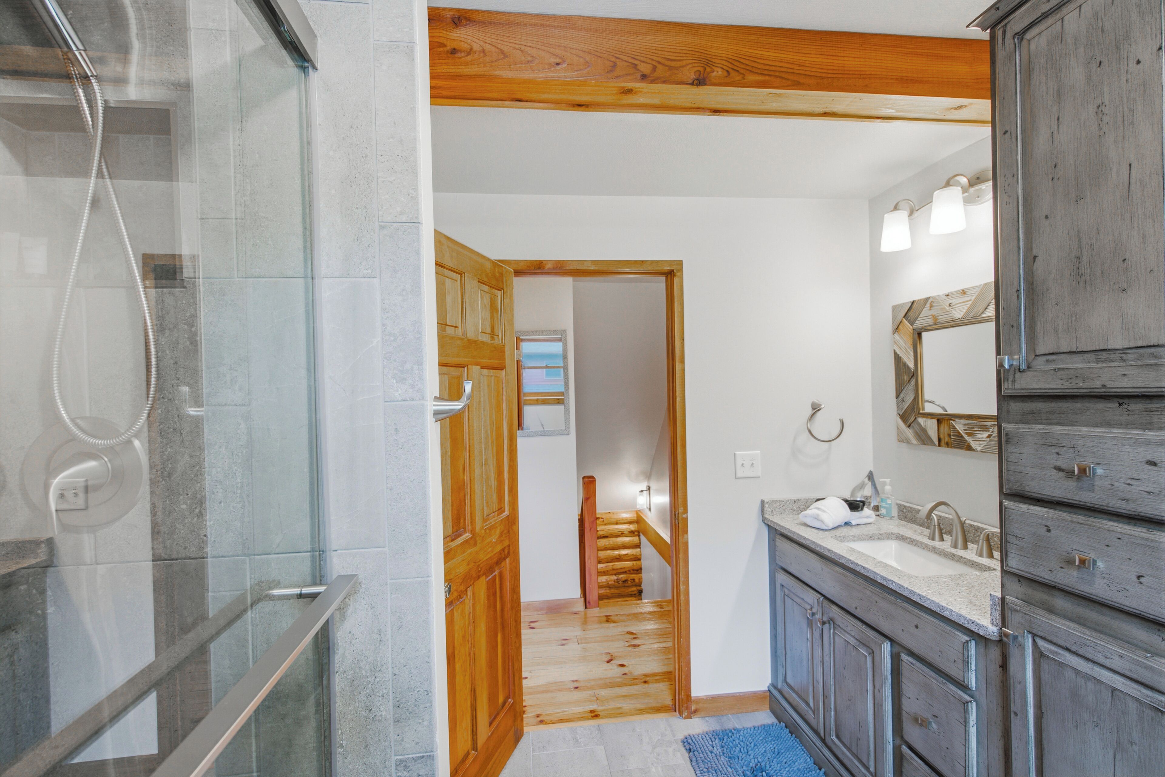 Un baño con cabina de ducha de vidrio, puerta de madera y tocador con espejo.