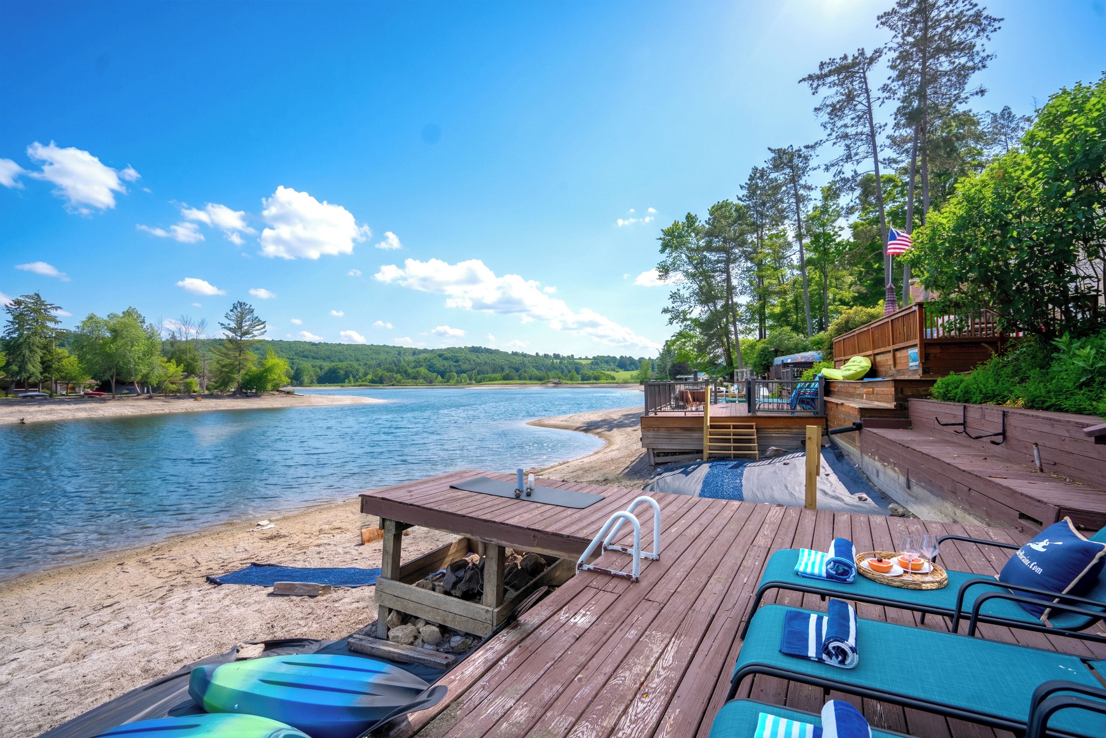 Een houten terras met lounge stoelen en een zwembadje, met uitzicht op een rivier en omgeven door groen.