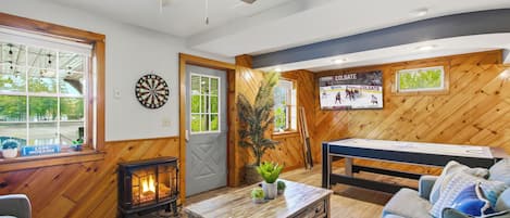 Una habitación acogedora con piso de madera, ventilador de techo, dardos, mesa de billar y chimenea.