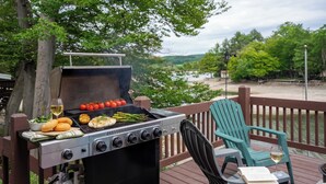Un barbecue en plein air avec des légumes et de la viande, une chaise et un verre de vin sur une terrasse.