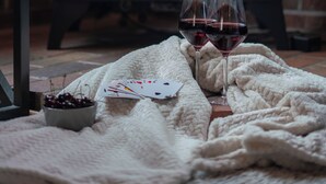 Une pièce chaleureuse avec une cheminée, une couverture et deux verres de vin rouge.