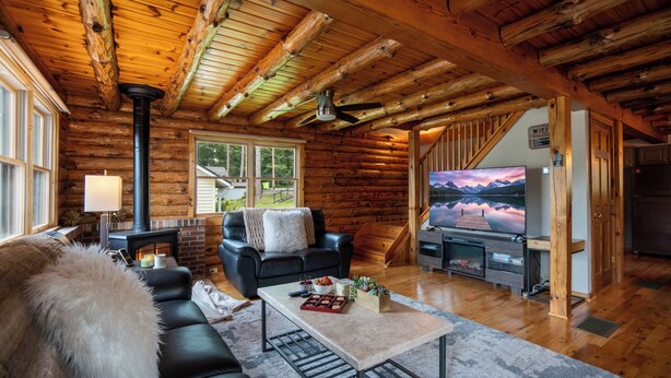 L’intérieur d’une cabane en rondins, avec une cheminée, un téléviseur et un coin salon confortable.