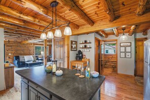 A rustic cabin interior with a kitchen island, wooden ceiling beams, and a dining area.