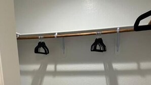 Een kast met een houten stang en zwarte ophanghaakjes.