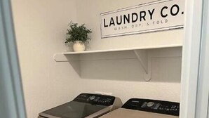 Een wasruimte met twee wasmachines en een plank erboven met de tekst 'LAUNDRY CO. WASH, DRY & FOLD'.