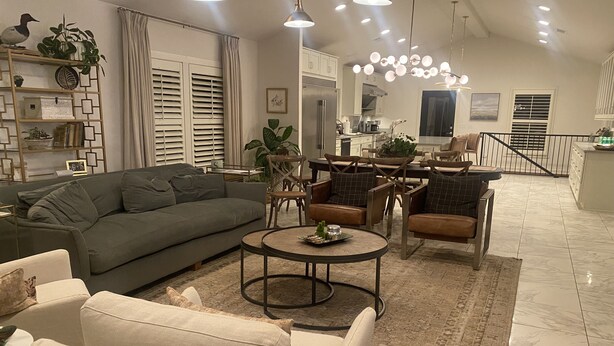 A modern living room with a sectional sofa, armchairs, a coffee table, and a dining area with a chandelier.