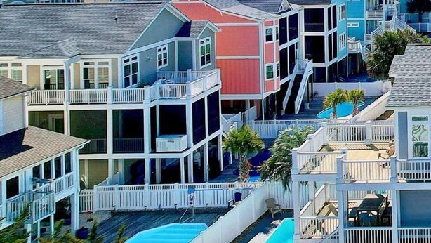 A coastal residential area with colorful houses, a swimming pool, and a view of the ocean.
