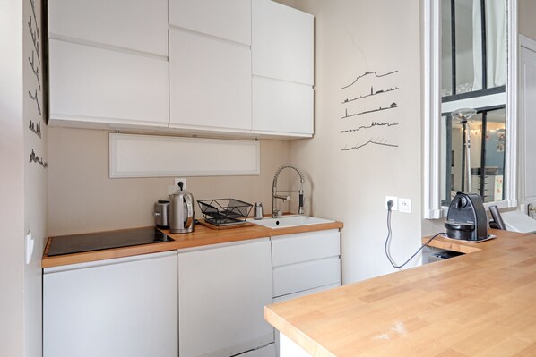 A modern kitchen with white cabinets, a wooden countertop, a kettle, a coffee maker, and a window with curtains.