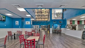 A spacious dining area with multiple tables and chairs, a staircase leading to an upper level, and a view of the outside through large windows. - Sand Dunes 2745 (Myrtle Beach)