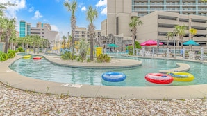 A pool area with multiple lanes, palm trees, and a hotel building in the background. - Sand Dunes 2745 (Myrtle Beach)
