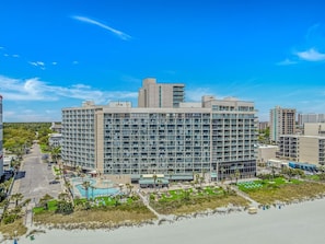 A modern hotel with multiple floors, a swimming pool, and a beachfront view.