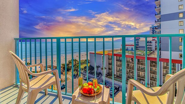 A balcony with chairs, a table with fruit and drinks, and a view of the beach and ocean. - Sand Dunes 2745 (Myrtle Beach)