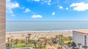 A beach view from a balcony with a pool and palm trees.