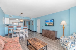 A compact living space with a dining area, kitchenette, and a TV mounted on the wall.