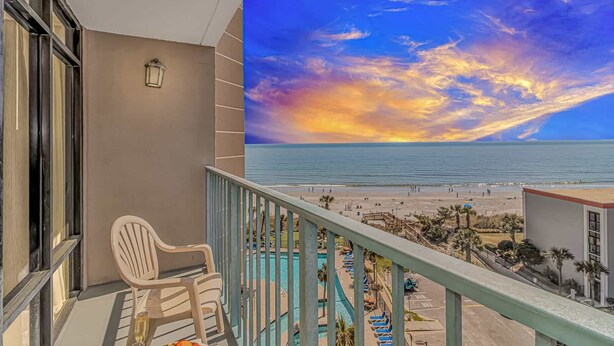 A balcony with a view of the beach and ocean during sunset.