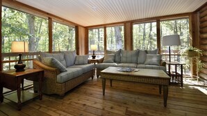 Interior de uma cabana de madeira com uma janela grande, um sofá, uma mesa de centro e um abajur.