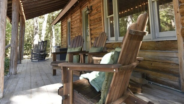 Uma cabana de madeira com varanda coberta, cadeiras de balanço e uma mesa.