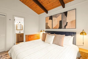 Una camera da letto con un letto, una testiera in legno, opere d'arte astratte alle pareti, abat-jour e un comò in legno.