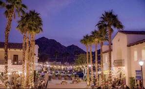 An outdoor dining area with palm trees, string lights, and a mountain backdrop.