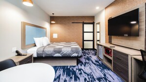 A modern hotel room with a bed, a desk, a television, and a microwave. - Palace Inn (Humble)