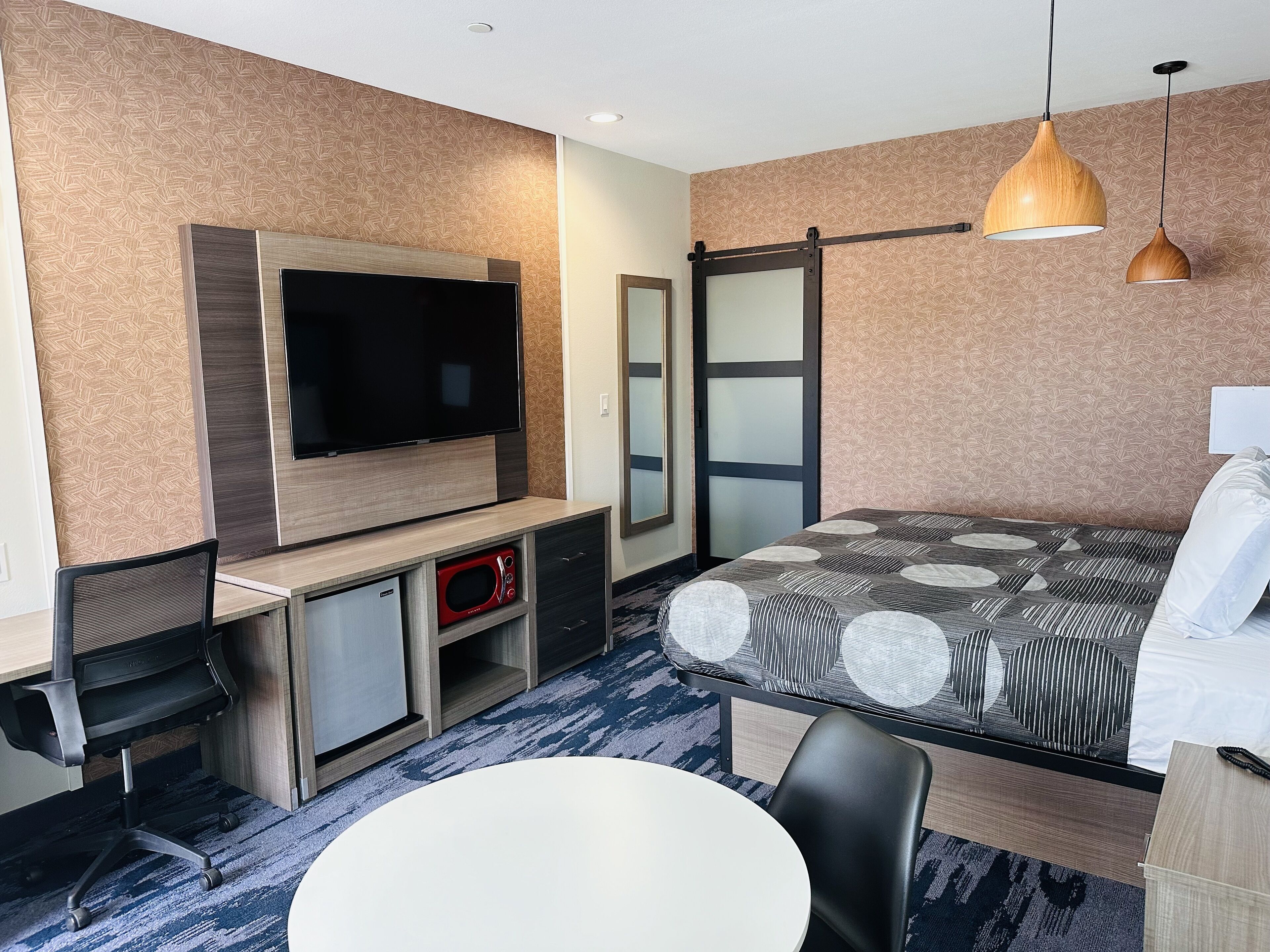 Hotelkamer met flatscreen televisie, een bed met beddengoed met dessin, een bureau met computer en magnetron, en een zithoek met tafel en stoelen.