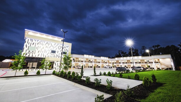 A modern hotel with a multi-story structure, a parking lot, and a well-maintained lawn. - Palace Inn (Humble)