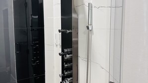 A modern bathroom with a curved showerhead, multiple faucets, and a glass shower enclosure. - Palace Inn (Humble)