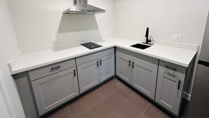 A modern kitchen with white cabinetry, a stainless steel range hood, and a double sink. - Palace Inn (Humble)
