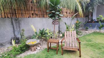 Un banco y una mesa de madera en un jardín con valla de bambú y diversas plantas.
