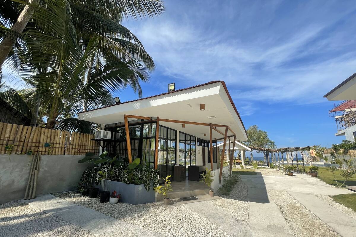 Una casa moderna amb un porxo cobert, un camí de formigó i vistes al mar.