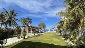 Un jardín tropical con una pérgola, palmeras y vista al mar.