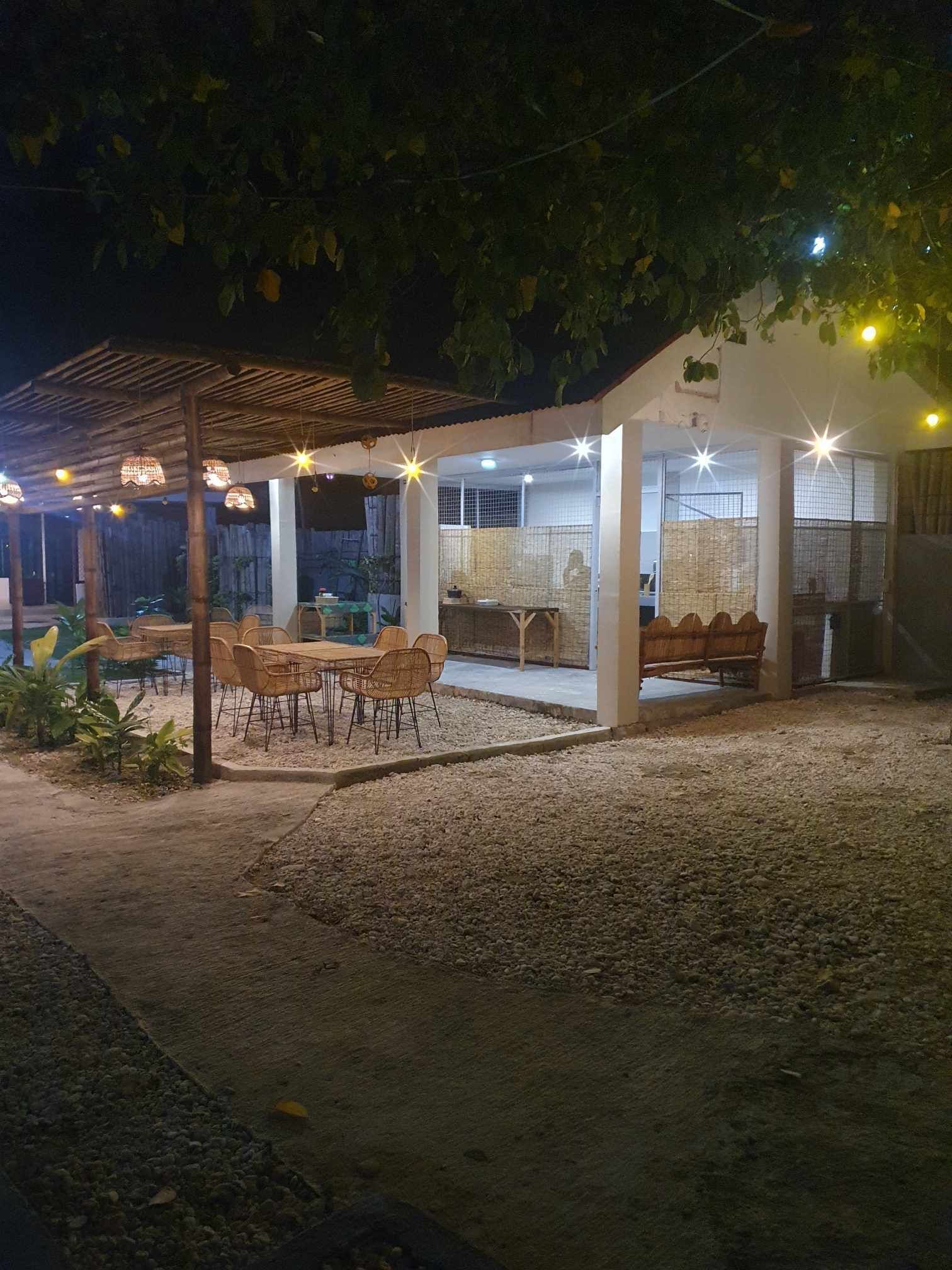 Un patio extérieur couvert, doté de tables et de chaises, d’un espace détente avec des coussins et d’une clôture décorative.
