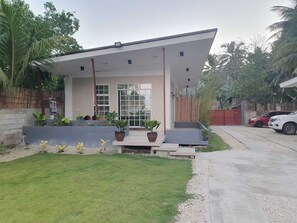 Una casa moderna con techo plano, ventanas grandes y un pequeño porche con plantas en macetas.