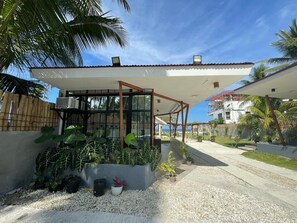 Una casa moderna con un porche cubierto, grandes ventanales y un jardín con diversas plantas.