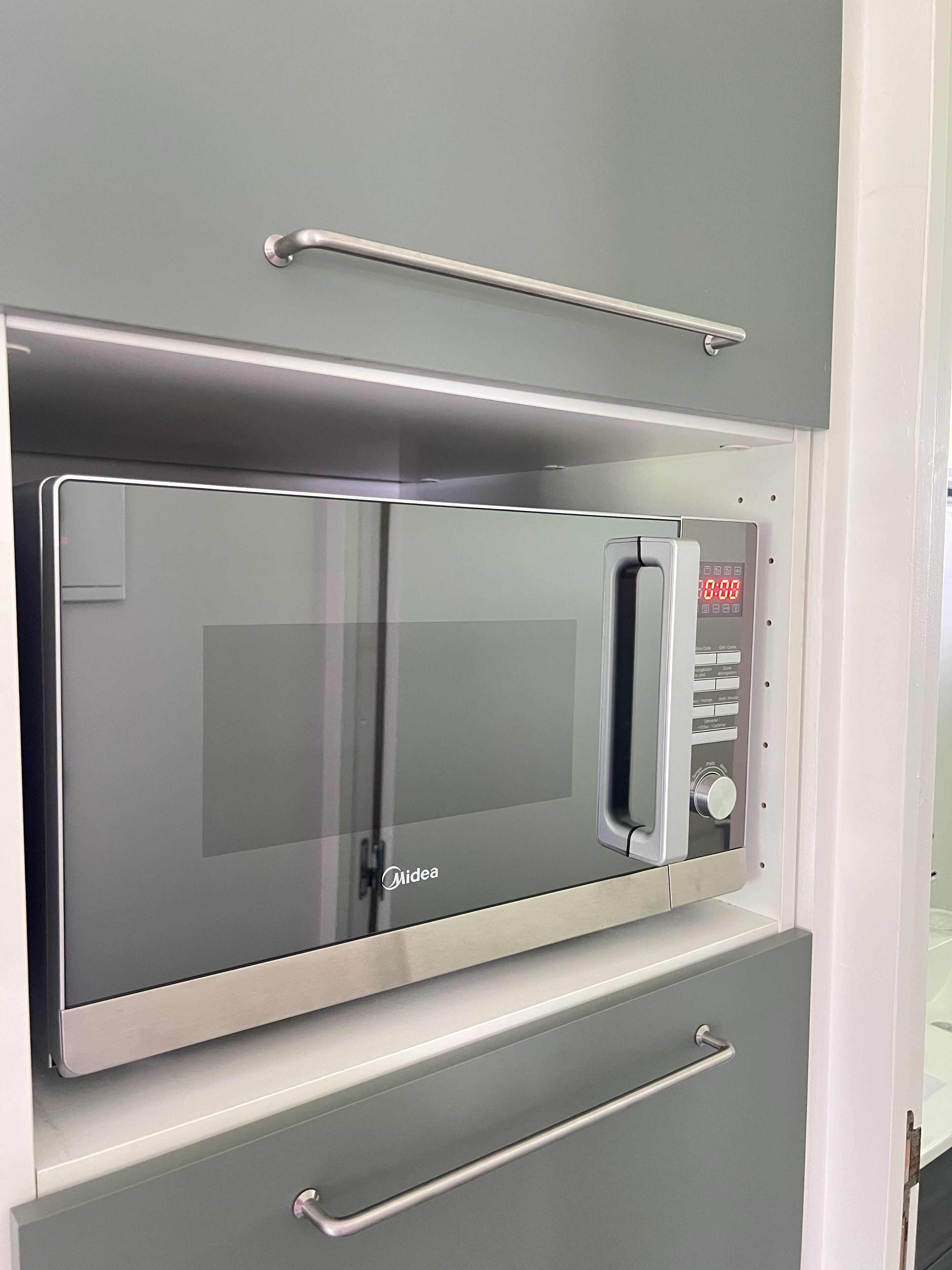Een moderne keuken met een inbouwmagnetron, een roestvrijstalen oven en een handgreep voor gemakkelijke toegang.