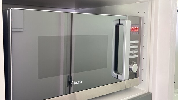 Una cocina moderna con microondas integrado, horno de acero inoxidable y un tirador para facilitar el acceso.
