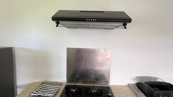 Une cuisine équipée d’une cuisinière à gaz, d’une hotte aspirante et d’un égouttoir à vaisselle.