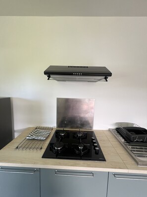 A kitchen with a gas stove, a range hood, and a dish rack. - Âpara Feti'a - Mirimiri Lodge (Raiatea)