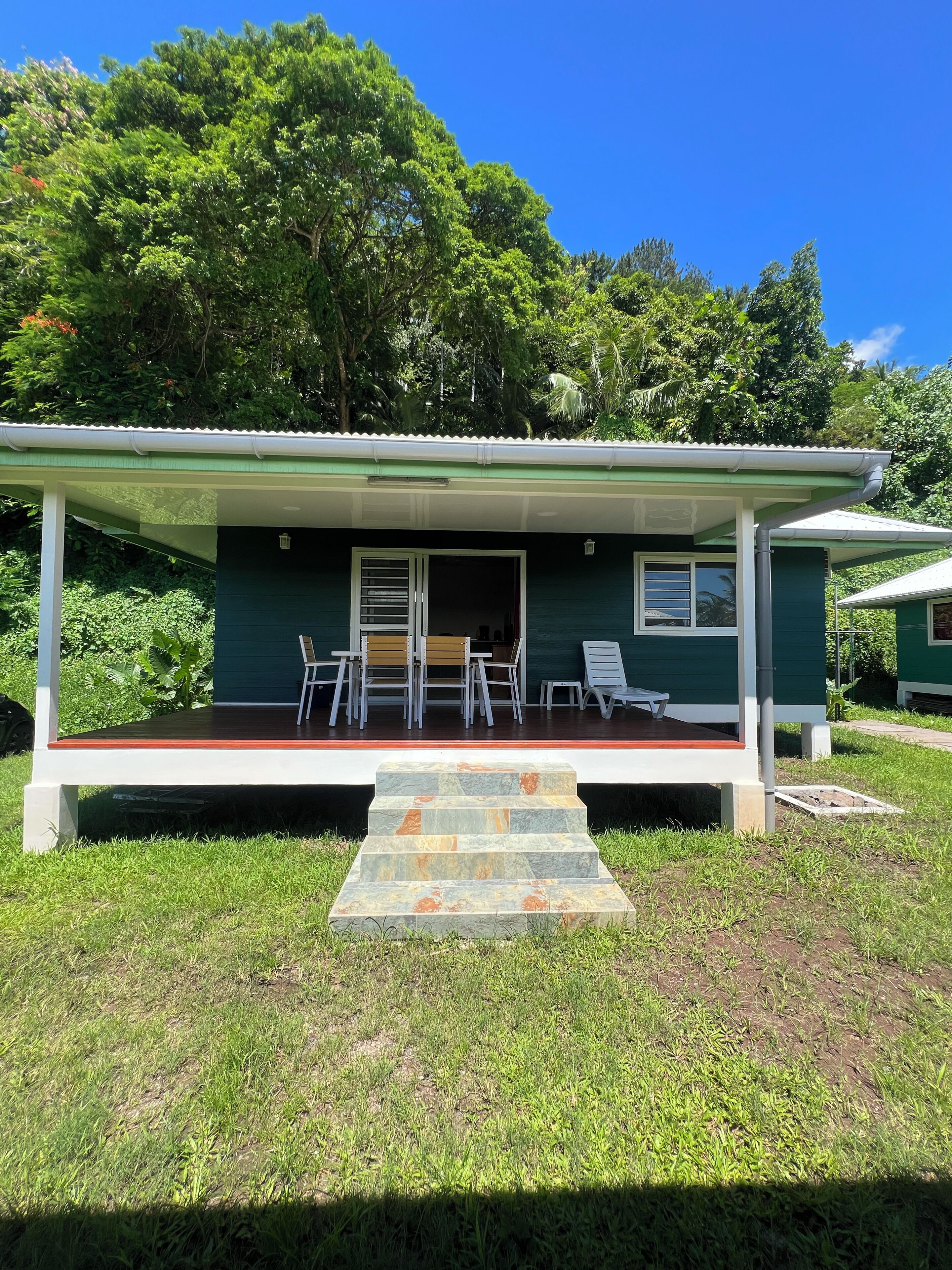 Uma casa verde com varanda coberta, área de estar externa e escadaria de pedra que leva à entrada.