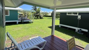 Un patio techado con dos sillones blancos y una silla de madera. Se ve una casa móvil verde al fondo.