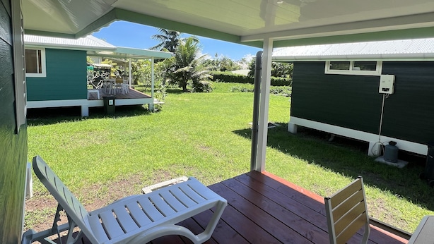 Een overdekt terras met twee witte loungesteilen en een houten stoel. Een groene stacaravan is op de achtergrond zichtbaar.