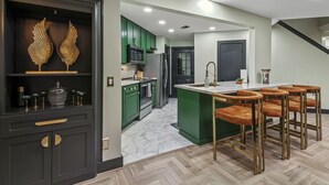 Una cocina moderna con gabinetes verdes, piso de mármol y una isla central con taburetes de bar.