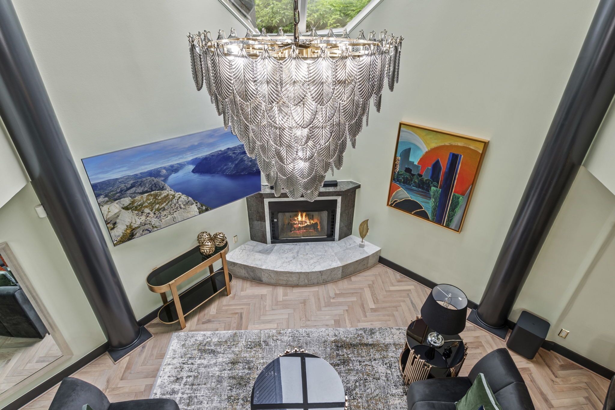 A modern living room with a fireplace, a large chandelier, and artwork on the walls.