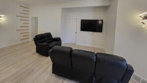 Una sala de estar moderna con un sofá de cuero negro, un televisor de pantalla plana montado en la pared y un adorno mural de listones de madera.