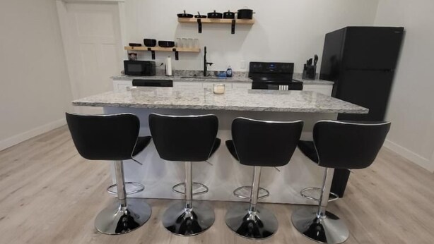 Una cocina moderna con una isla central, cuatro taburetes negros y un refrigerador negro.