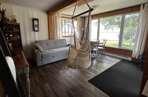 Una sala de estar con sofá gris, pisos de madera, una silla colgante, una estantería de madera y un ventanal con cortinas.